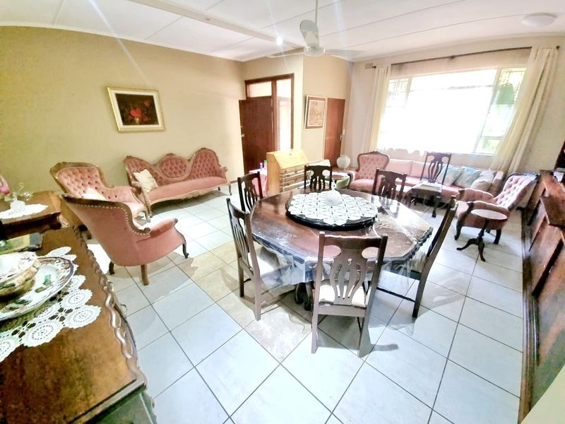 A spacious living and dining area featuring neutral tiled flooring, a ceiling fan, and large windows that provide ample natural light.
