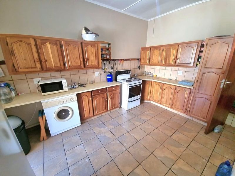 A functional kitchen featuring wooden cabinetry, tiled flooring, laminate countertops, and a freestanding stove, offering a traditional layout with ample storage space.