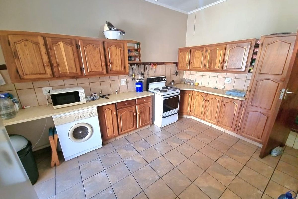 A functional kitchen featuring wooden cabinetry, tiled flooring, laminate countertops, and a freestanding stove, offering a traditional layout with ample storage space.