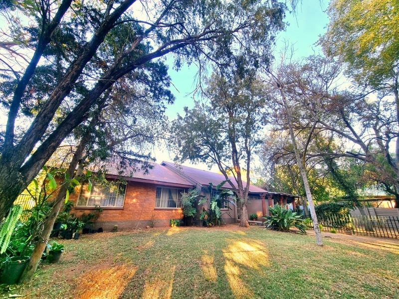 Front view of a single-story brick house featuring a metal roof, surrounded by a spacious lawn and mature trees.
