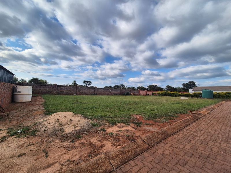 A vacant residential plot featuring a paved driveway, perimeter brick boundary wall, and an existing water storage tank.