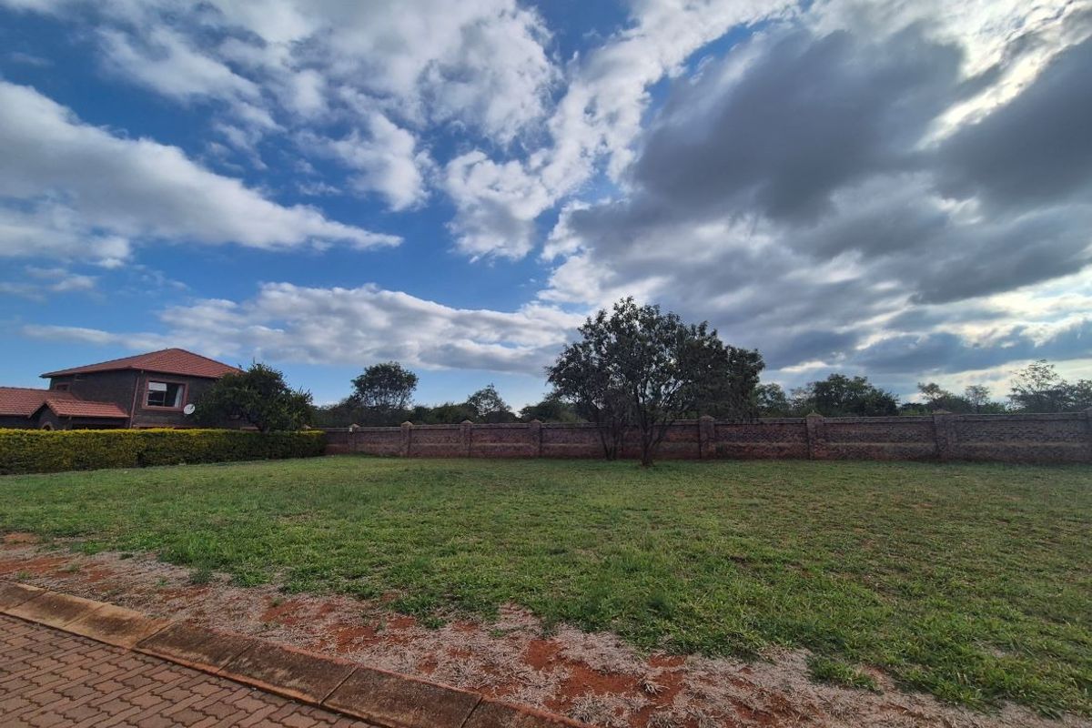 A vacant residential plot featuring a brick boundary wall, established tree, and paved verge, offering a clear space for potential development.