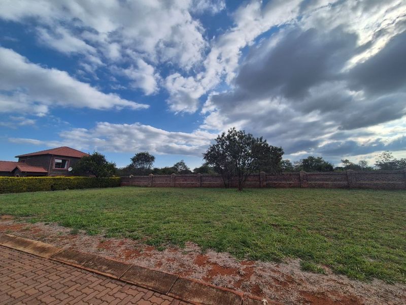 A vacant residential plot featuring a brick boundary wall, established tree, and paved verge, offering a clear space for potential development.