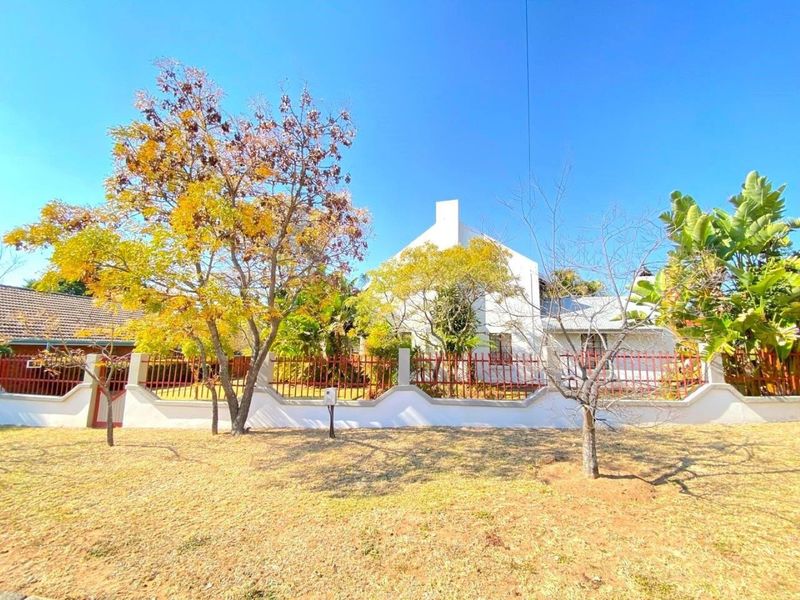 Front view of the property featuring a white facade, chimney, and a secure perimeter wall with metal fencing.