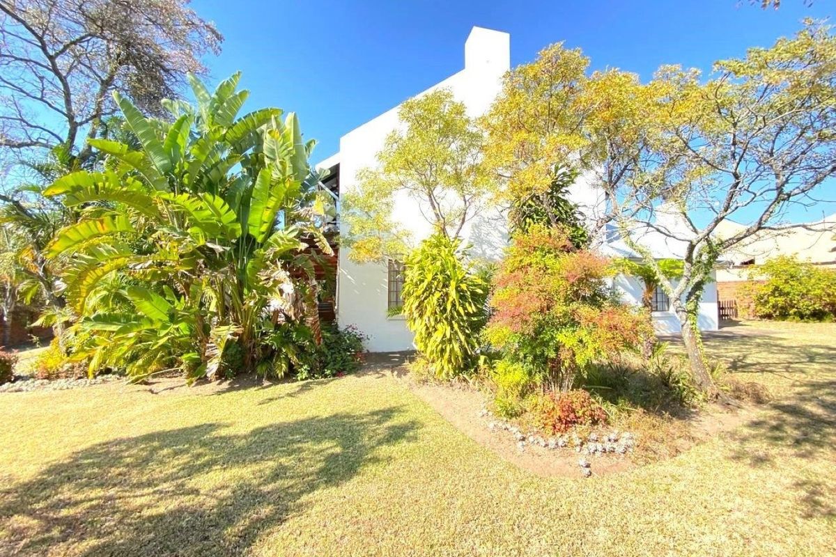 A view of the rear exterior of the house featuring a white facade, a prominent chimney, and a well-maintained garden area.
