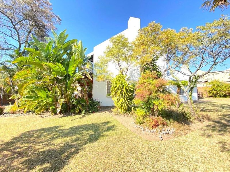 A view of the rear exterior of the house featuring a white facade, a prominent chimney, and a well-maintained garden area.