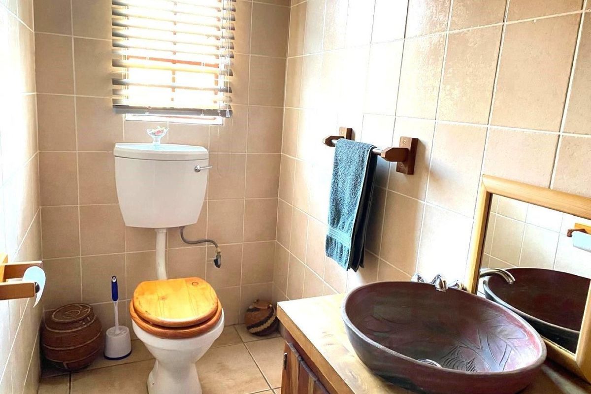 A compact bathroom featuring ceramic wall and floor tiles, a wooden vanity with a decorative vessel sink, and a standard toilet.