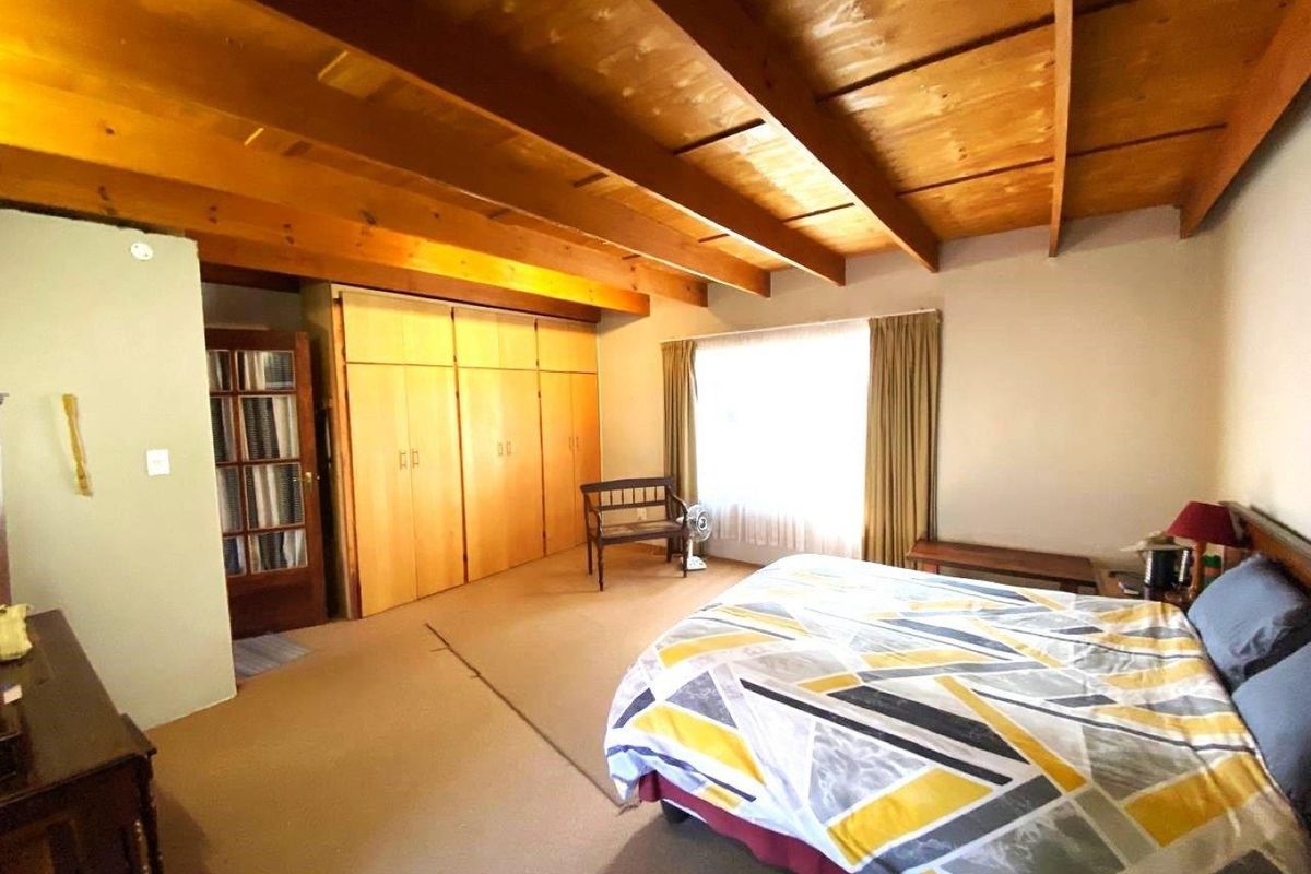 Spacious bedroom featuring a distinctive exposed timber beam ceiling and extensive built-in wooden cabinetry for ample storage.