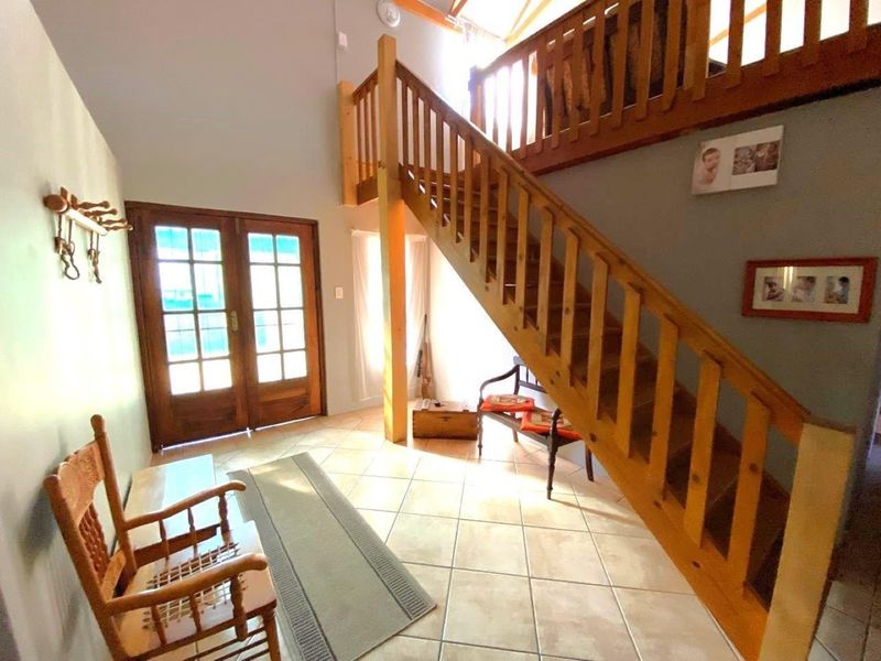 Entrance hall featuring a double-height ceiling, tiled flooring, and a prominent wooden staircase leading to a mezzanine level.