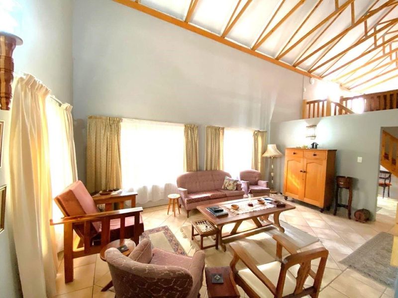Spacious living room featuring a high vaulted ceiling with exposed timber trusses, tiled flooring, and an open mezzanine level with a timber staircase.
