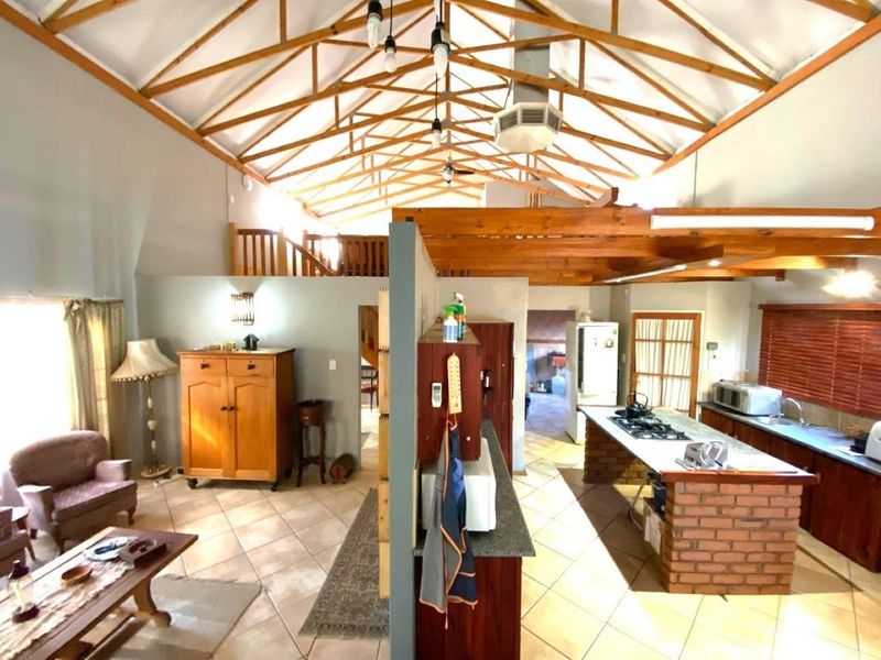 Spacious open-plan living and kitchen area featuring high exposed timber roof trusses, a brick kitchen island with gas cooktop, and a mezzanine level.