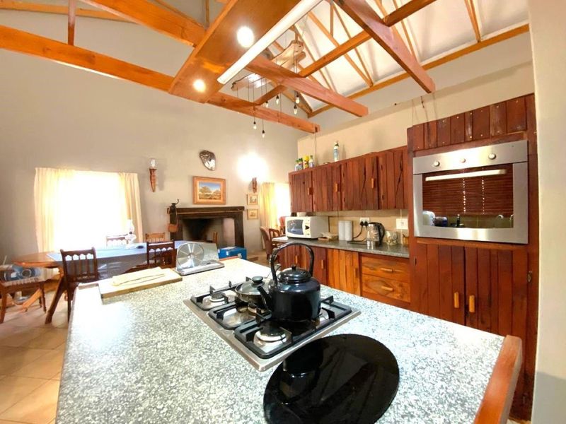 Open-plan kitchen and dining area featuring exposed timber roof trusses, a central island with gas hob, built-in oven, and a traditional fireplace.