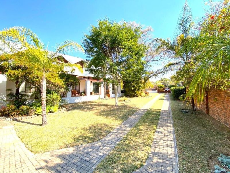 A well-maintained front exterior featuring a paved driveway, established garden, and a covered patio area leading to the main entrance.