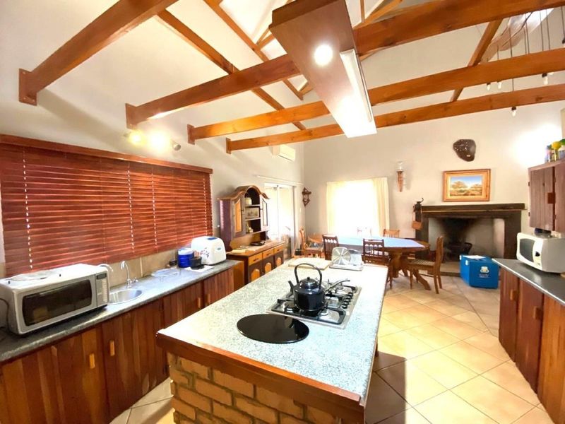 Spacious open-plan kitchen and dining area featuring exposed timber beams, a central island with gas hob, and a traditional built-in fireplace.