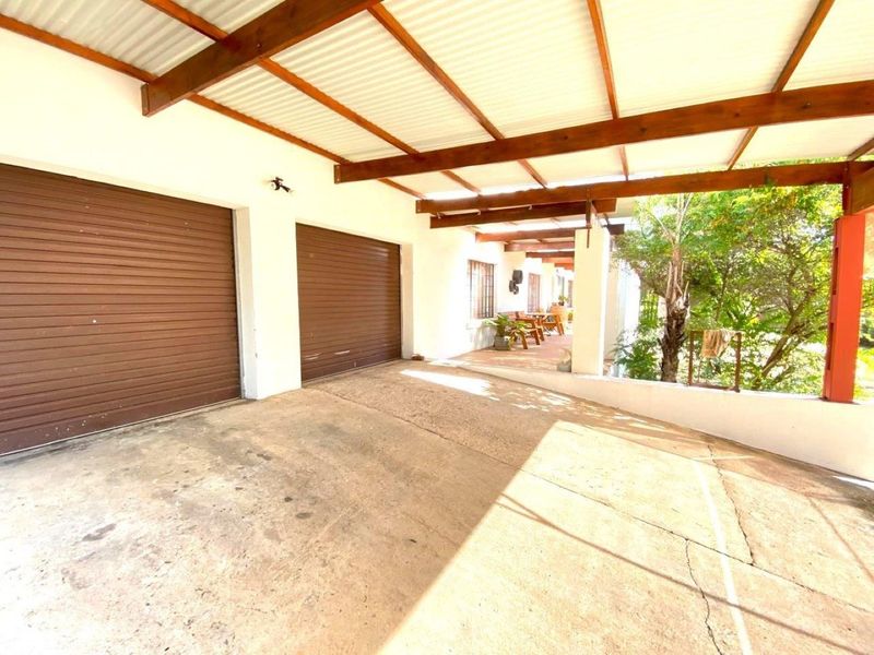 A covered double garage area with timber beam roofing and a concrete driveway, featuring an adjacent outdoor patio space.