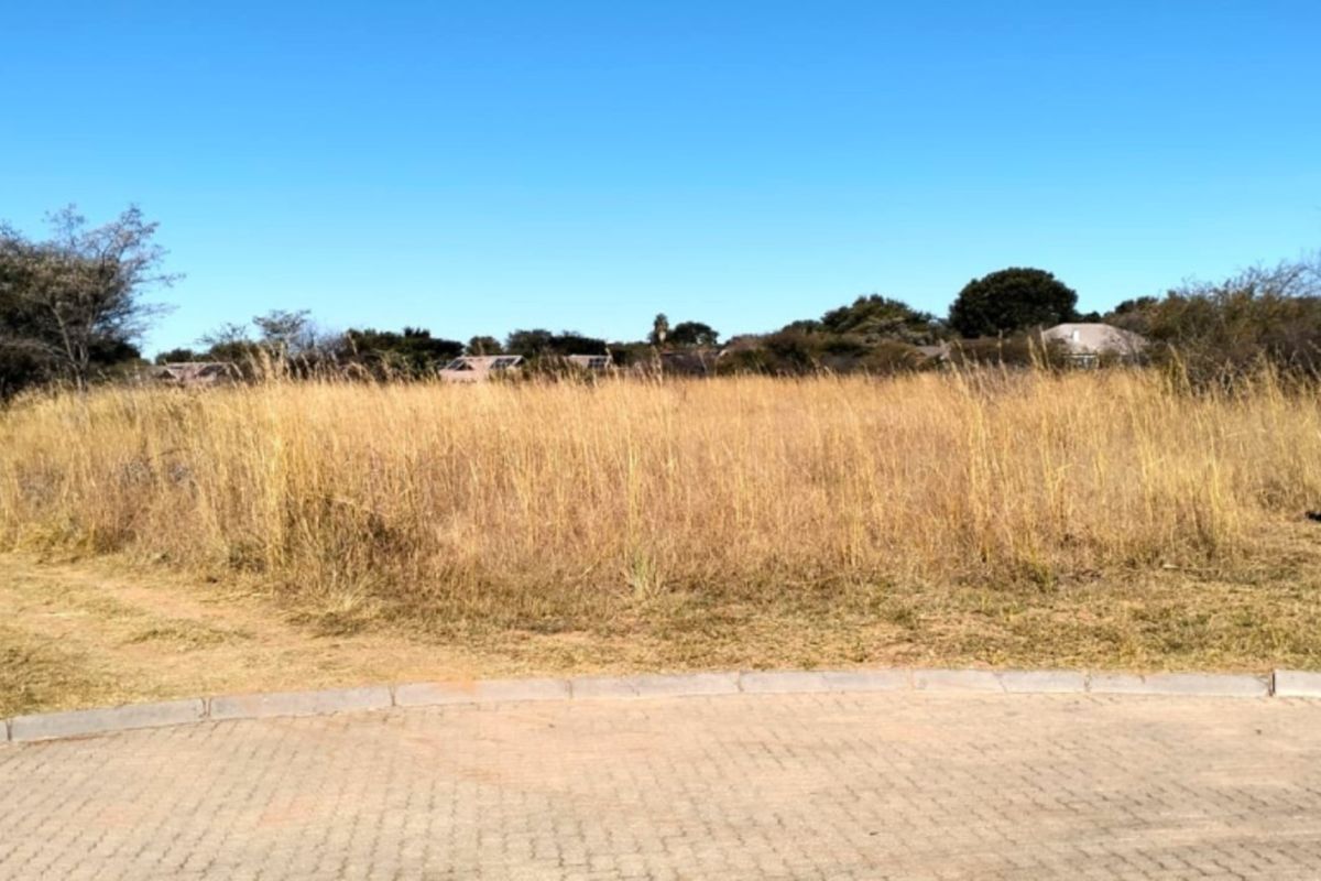 A vacant residential plot featuring natural grass cover and a paved curb, offering a clear view of the surrounding landscape.