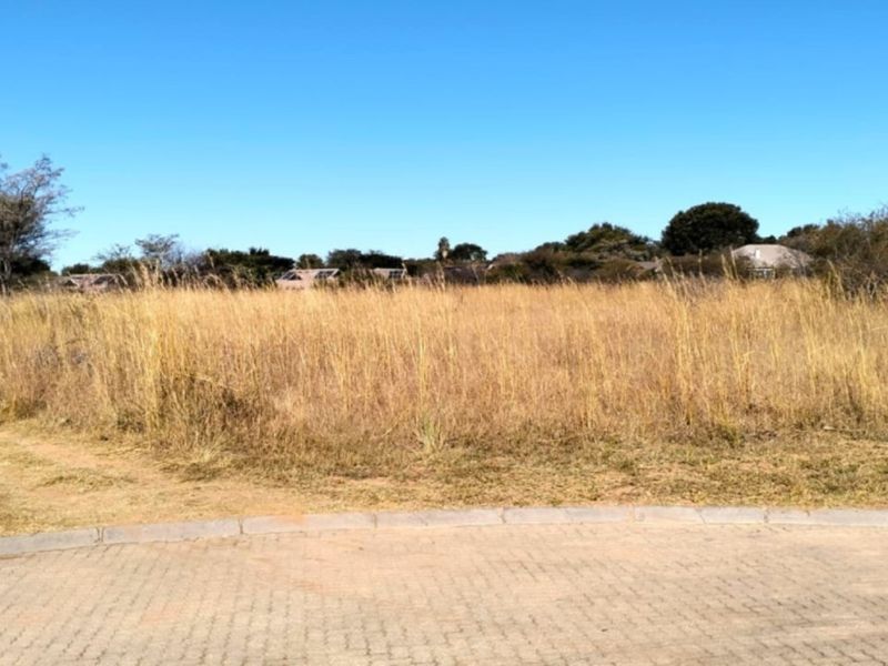 A vacant residential plot featuring natural grass cover and a paved curb, offering a clear view of the surrounding landscape.