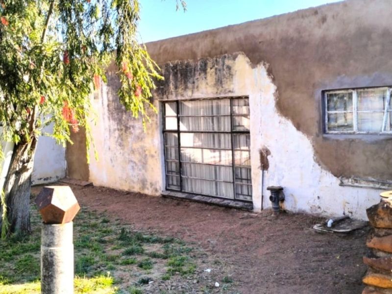 Rear exterior view of the farm building featuring stone masonry accents and plastered walls requiring maintenance and repainting.