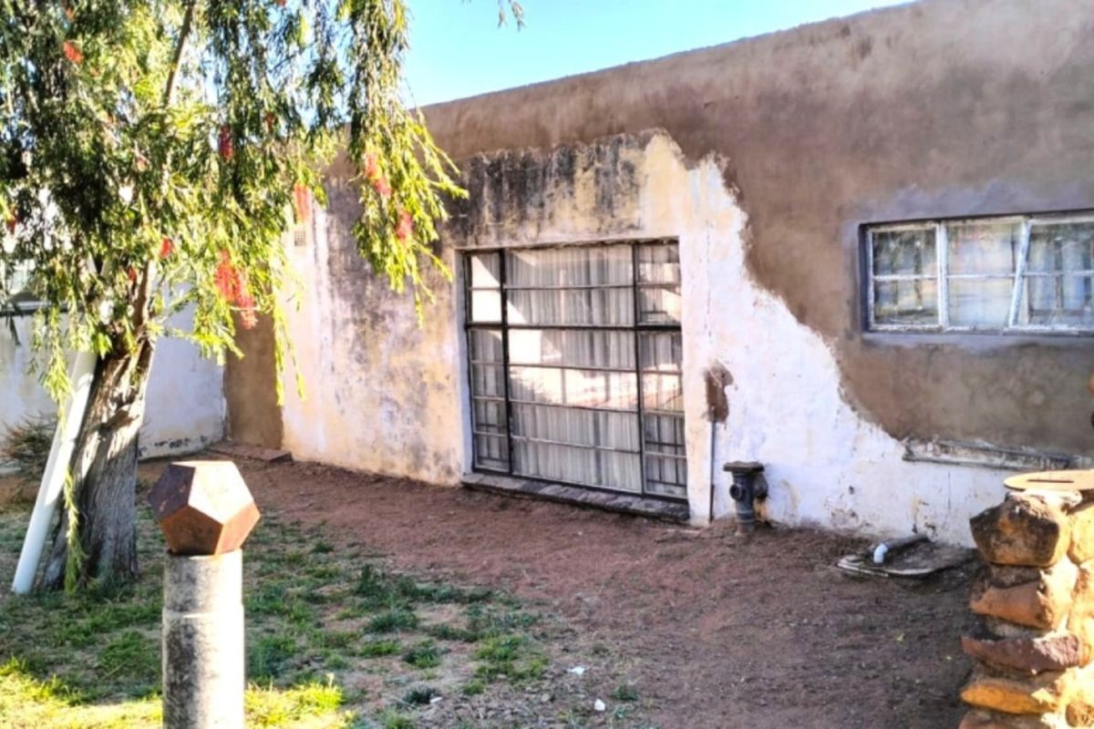 Rear exterior view of the farm building featuring stone masonry accents and plastered walls requiring maintenance and repainting.