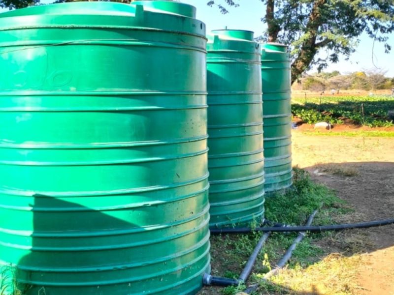 A set of green plastic water storage tanks connected to irrigation piping, situated on a farm property.