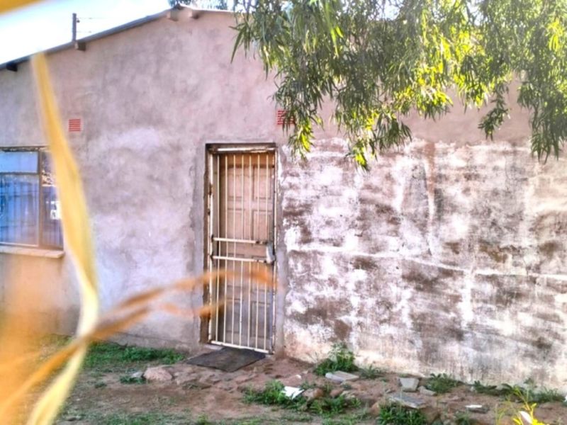 A view of the exterior front facade of a farm building featuring unfinished plaster walls and a security gate entrance.