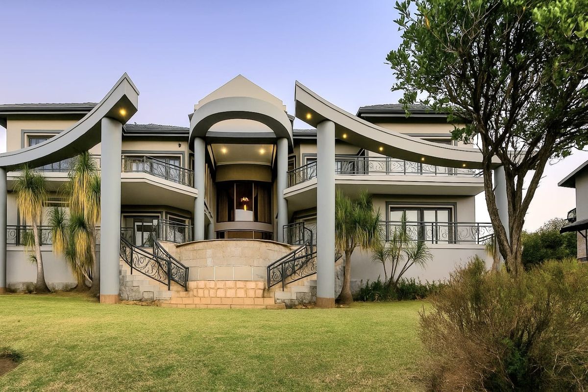A grand rear elevation featuring a prominent stone staircase, sweeping architectural arches, wrought iron balcony railings, and well-maintained landscaped grounds.