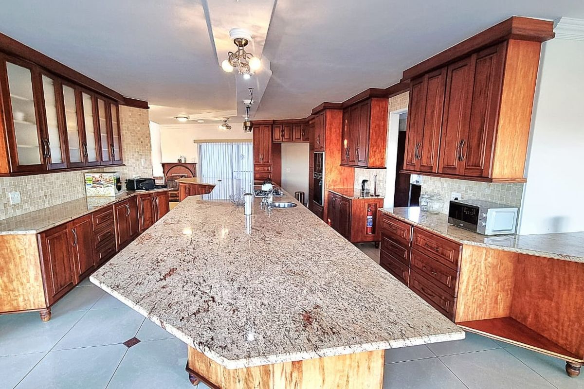 Spacious kitchen featuring extensive wooden cabinetry, a large central granite island, and tiled flooring, offering ample workspace and storage.
