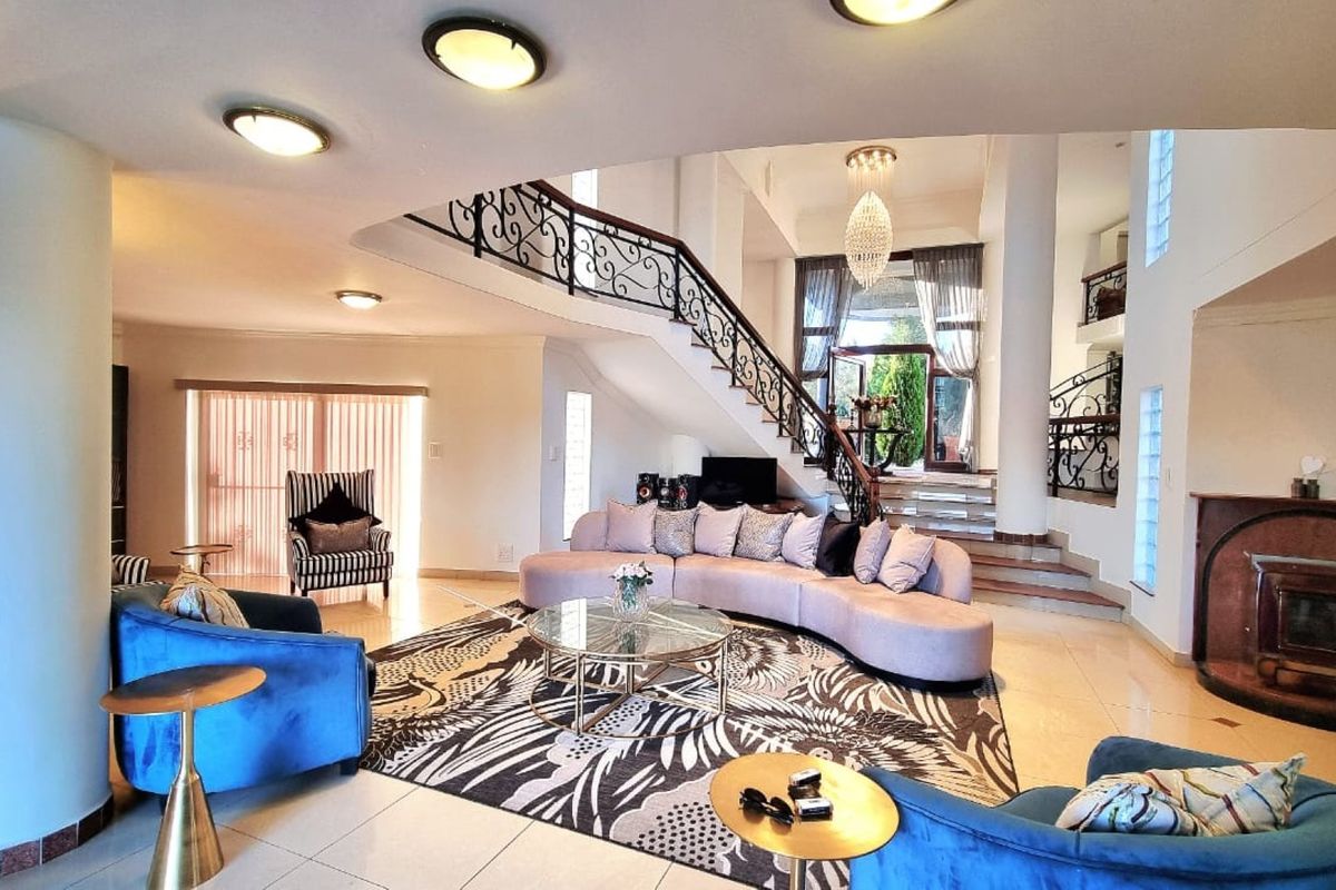 Spacious open-plan living area featuring a grand staircase with wrought iron detailing, a built-in fireplace, and elegant tiled flooring.