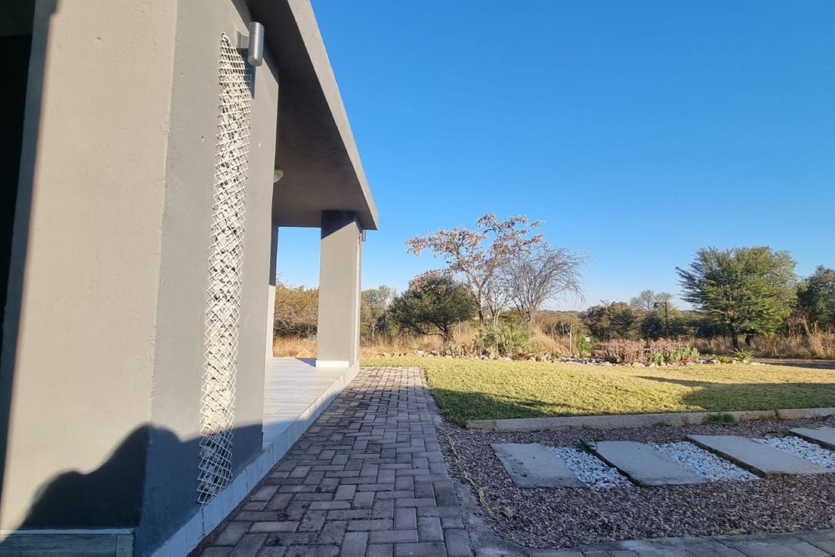 A view of the rear exterior featuring a covered patio, paved walkway, and a well-maintained garden area with natural landscaping.