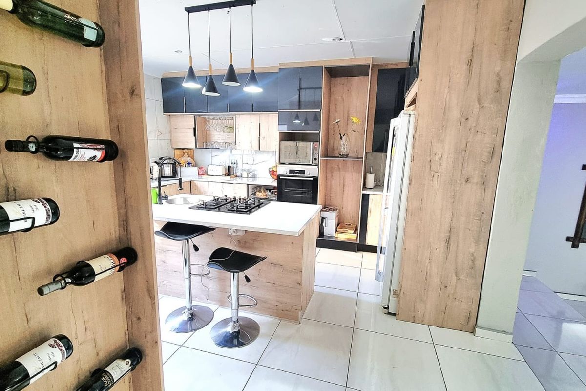 Modern kitchen featuring wood-look cabinetry, a central island with a gas hob, built-in appliances, and sleek tiled flooring.