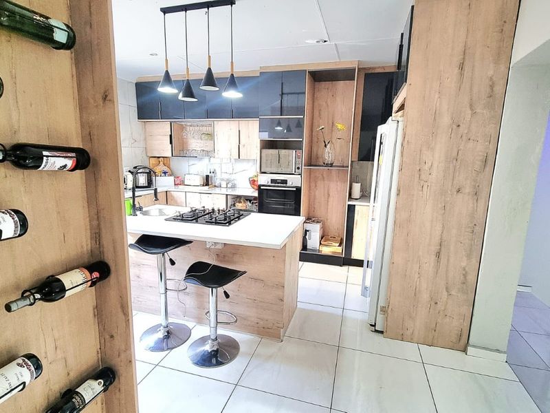 Modern kitchen featuring wood-look cabinetry, a central island with a gas hob, built-in appliances, and sleek tiled flooring.