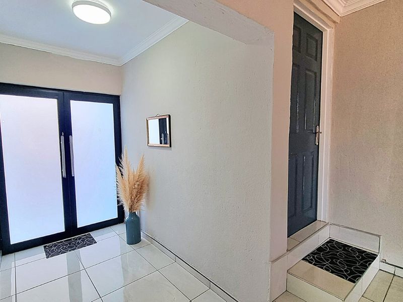 A bright and clean entrance hall featuring tiled flooring, a modern double glass front door, and a secondary internal door.