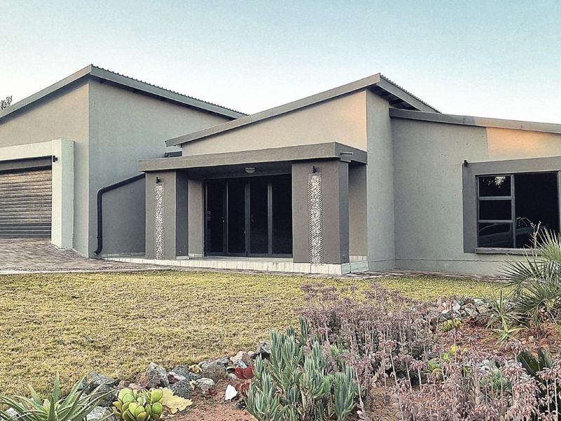 Modern single-story house featuring a grey facade, roller garage door, sliding glass entrance, and a well-maintained landscaped front garden.