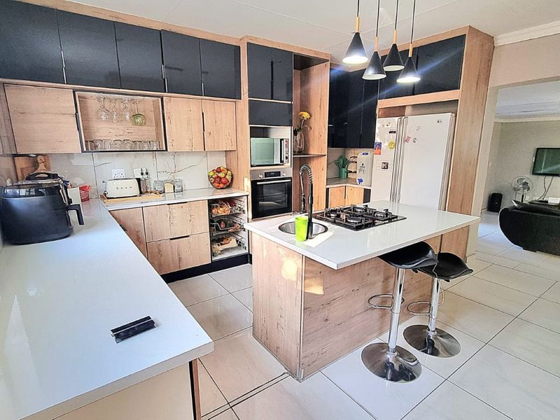 Modern open-plan kitchen featuring a central island with gas hob, sleek laminate cabinetry, quartz countertops, and integrated appliances, flowing into the living area.