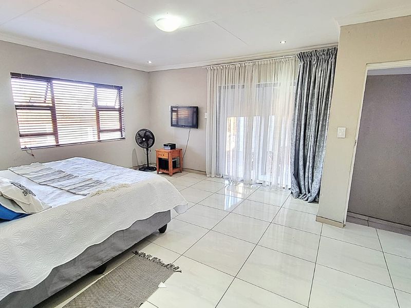 A spacious bedroom featuring neutral tiled flooring, recessed ceiling lighting, and a sliding glass door providing access to the exterior.