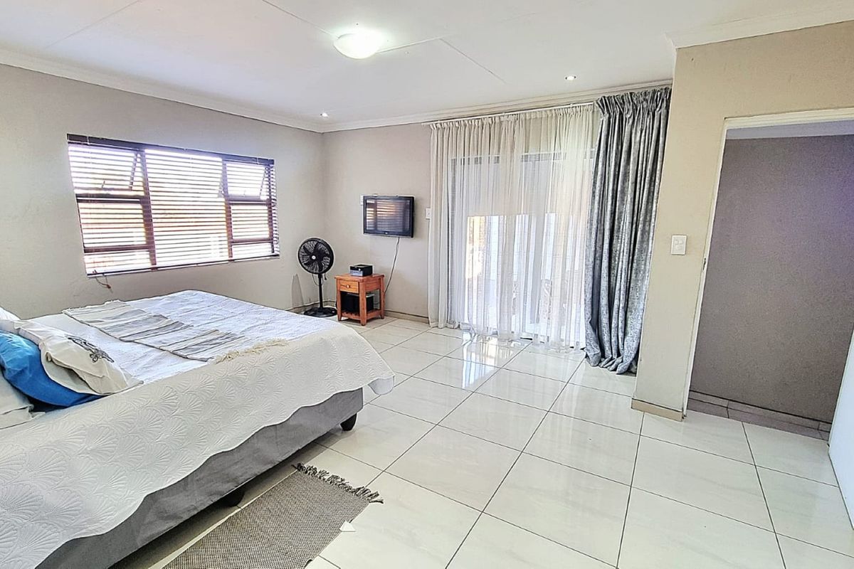 A spacious bedroom featuring neutral tiled flooring, recessed ceiling lighting, and a sliding glass door providing access to the exterior.