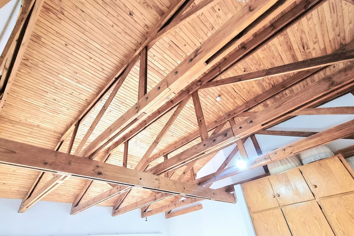 Spacious bedroom featuring high vaulted ceilings with exposed timber trusses and integrated wooden cabinetry.
