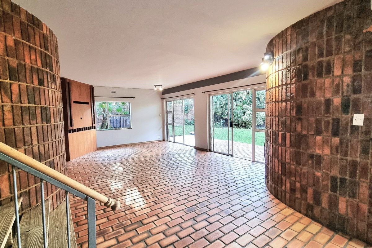 Spacious living area featuring unique curved brick walls, brick flooring, and large sliding glass doors providing direct access to the garden.