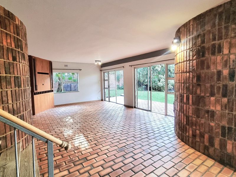 Spacious living area featuring unique curved brick walls, brick flooring, and large sliding glass doors providing direct access to the garden.