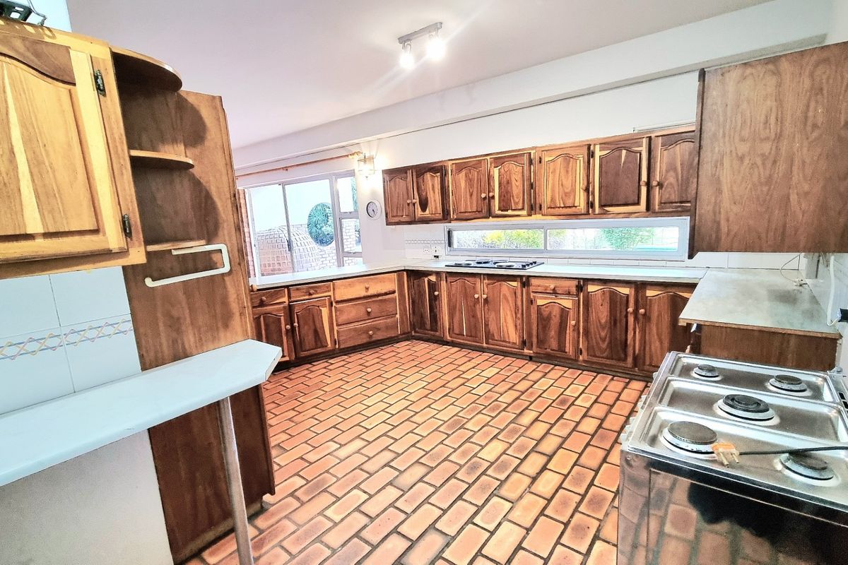 Spacious kitchen featuring extensive wooden cabinetry, a built-in gas hob, and traditional terracotta-style tiled flooring, offering a functional layout with ample storage space.