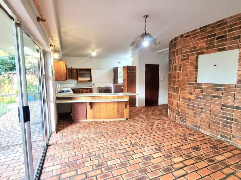 Open plan kitchen and living area featuring a distinctive curved brick feature wall, terracotta tile flooring, and direct access to the garden via sliding doors.