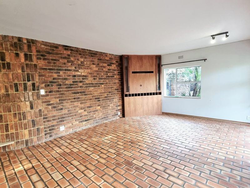 Spacious living area featuring a prominent exposed brick wall, built-in wooden cabinetry, brick flooring, and sliding glass doors leading to the exterior.