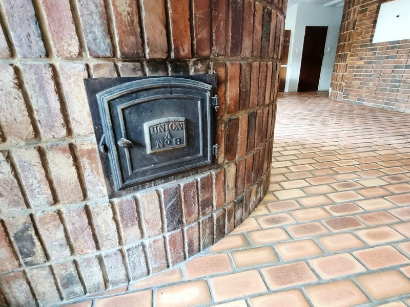 Spacious living area featuring a distinctive curved brick fireplace with a vintage cast iron door and matching brick flooring throughout.