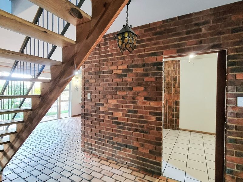 Entrance hall featuring an exposed brick feature wall, timber staircase, and tiled flooring, leading into an adjacent living space.