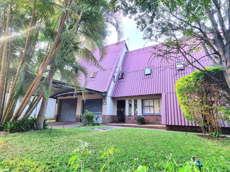 Front view of a unique A-frame style house featuring a prominent corrugated roof, brick exterior, double garage, and an attached carport.