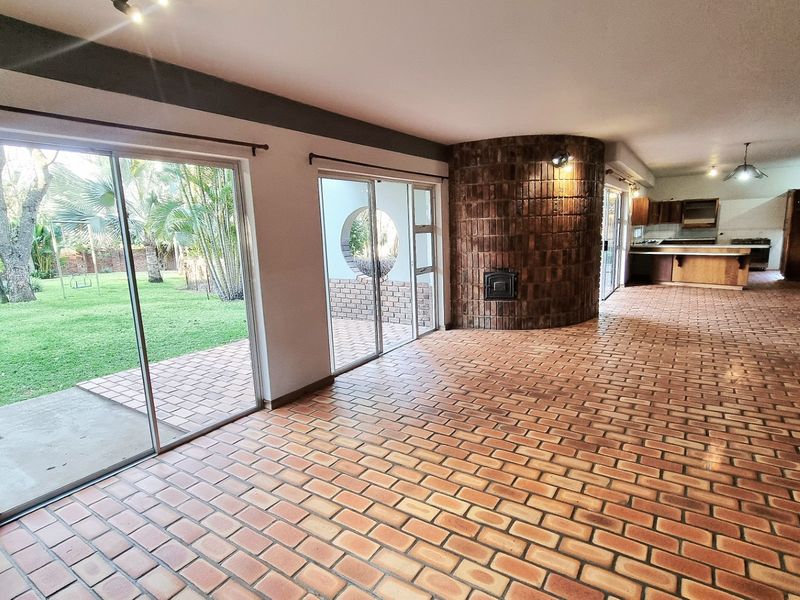 Spacious open-plan living and kitchen area featuring distinctive curved brick fireplace, terracotta brick flooring, and large sliding doors opening to the garden.