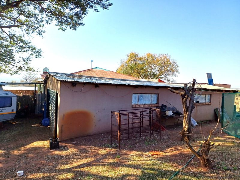 Rear view of a farm dwelling featuring plastered masonry walls and a corrugated metal roof, showing signs of weathering and maintenance requirements.