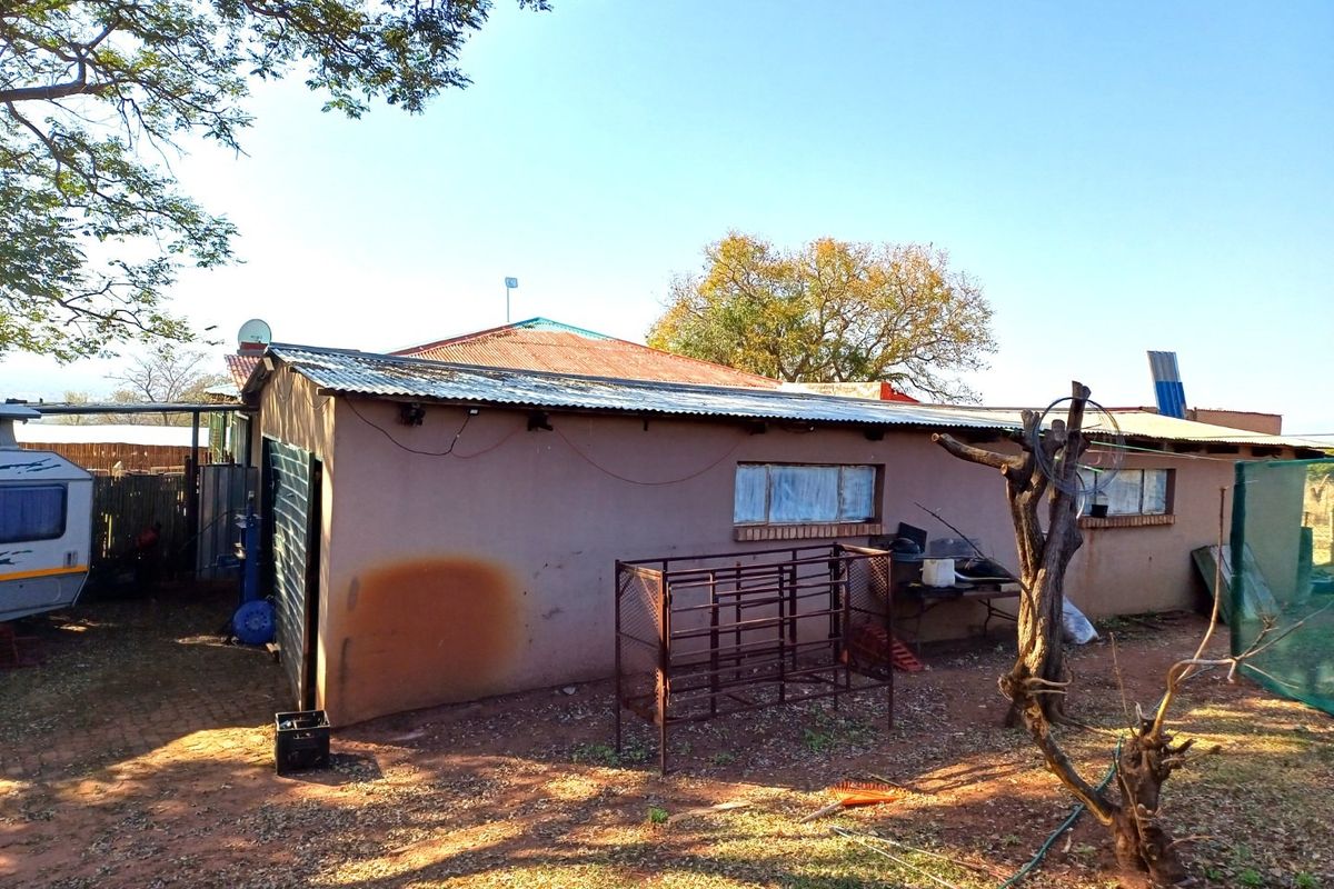 Rear view of a farm dwelling featuring plastered masonry walls and a corrugated metal roof, showing signs of weathering and maintenance requirements.