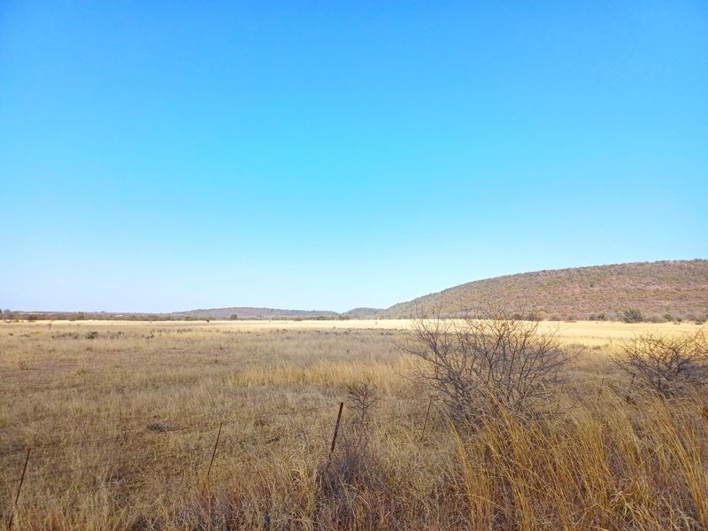 Expansive open farm landscape featuring dry grassland and distant hills, enclosed by simple wire fencing.