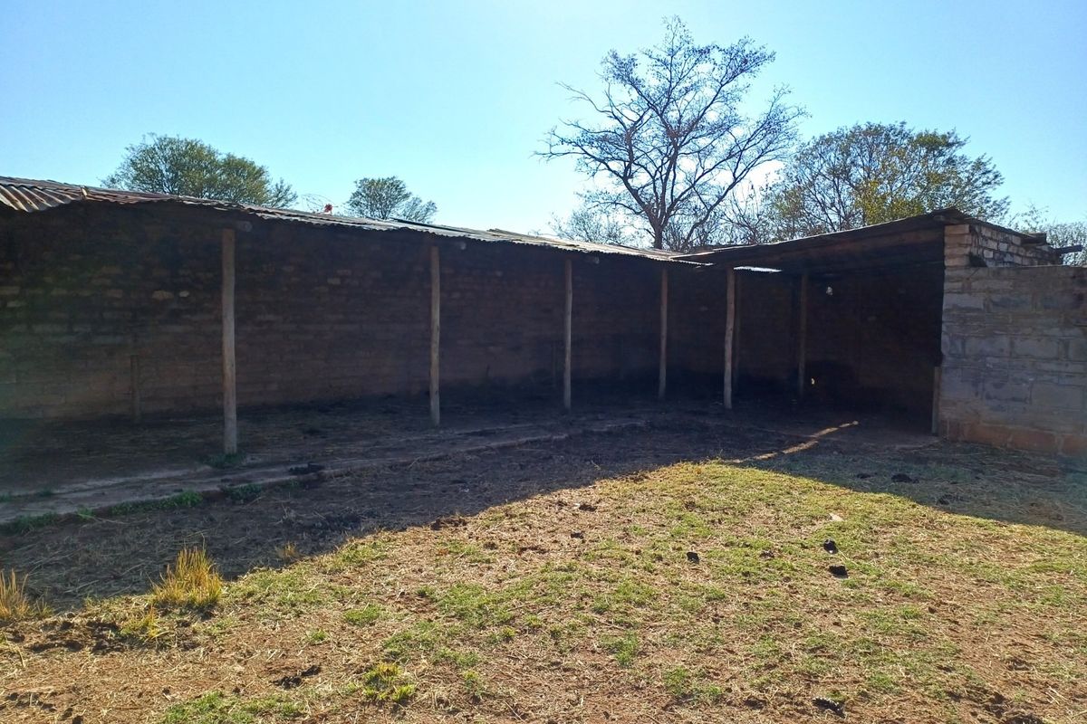 An open-sided farm utility structure featuring brick masonry walls and a corrugated metal roof supported by timber posts.